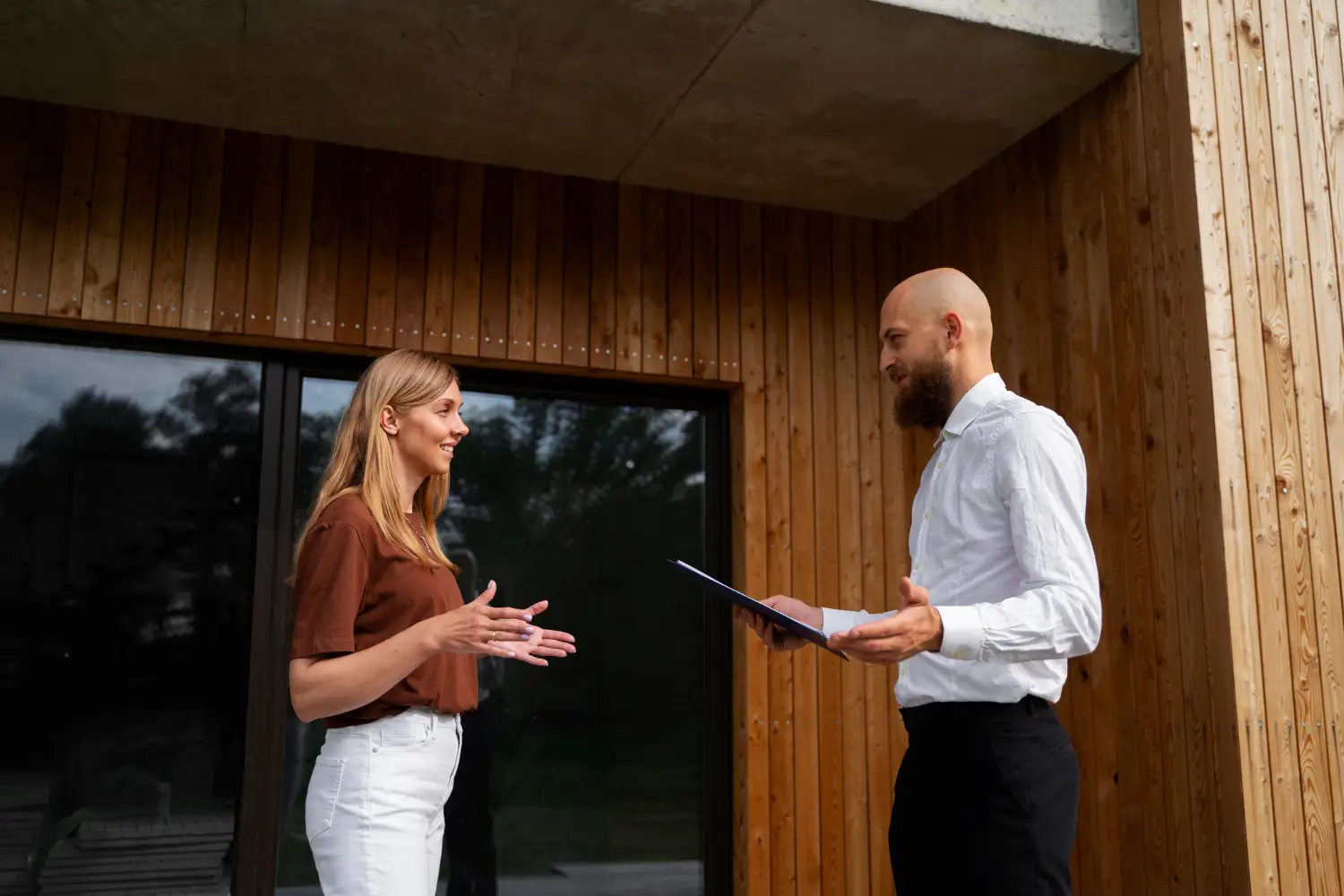 Two people talking in front of a wooden house